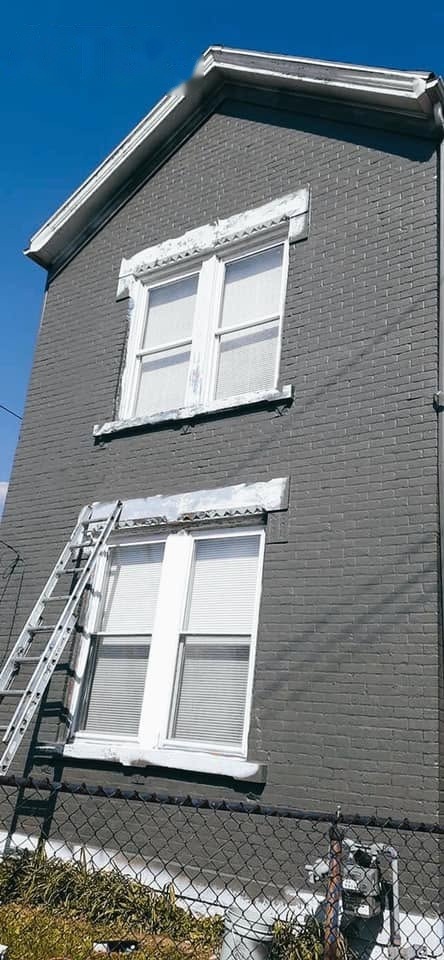 Brick building painted charcoal gray with white window trim and a ladder against the wall