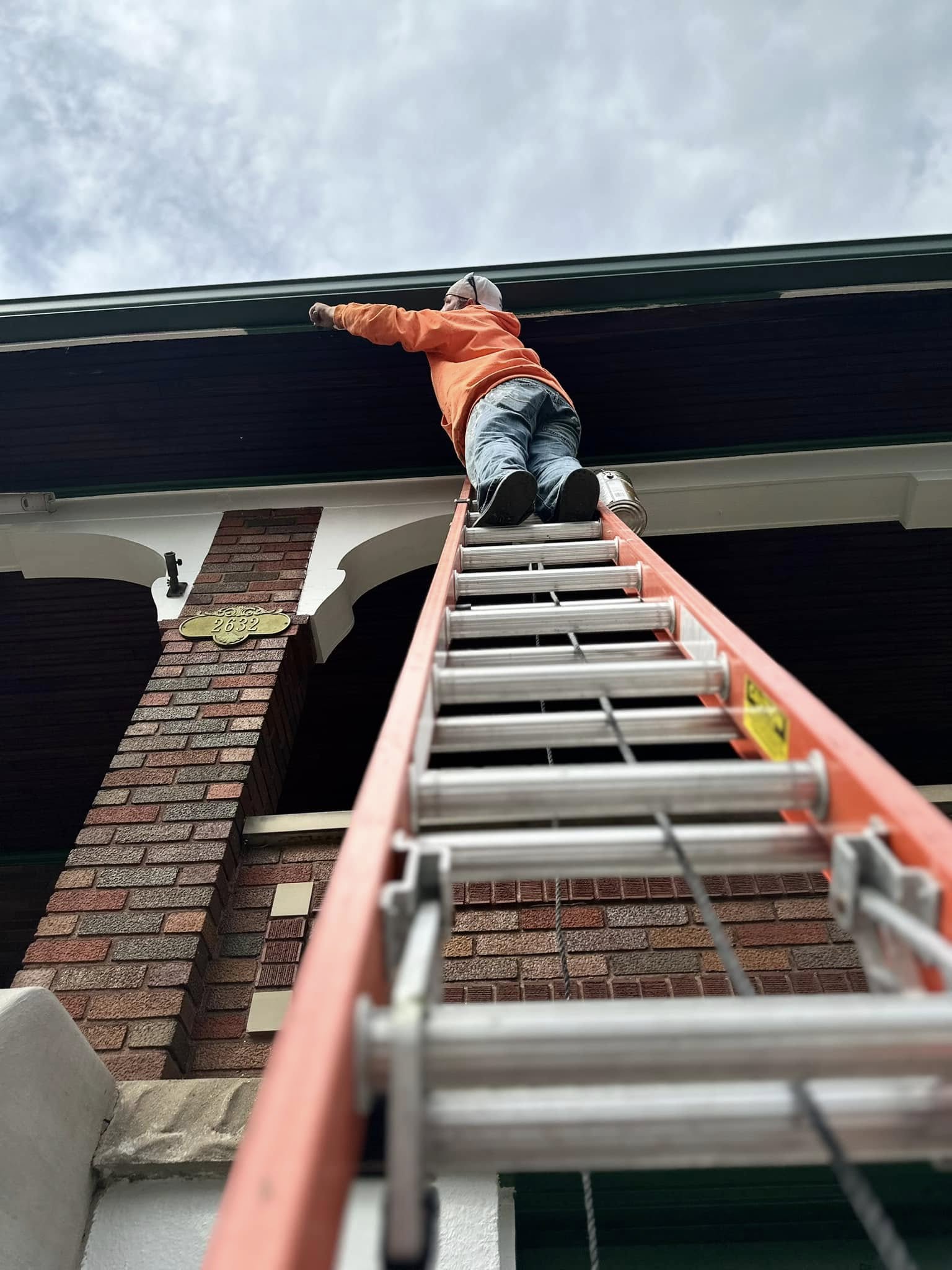 Dennis Kappes reaching to paint a fascia board from the top of an extension ladder.